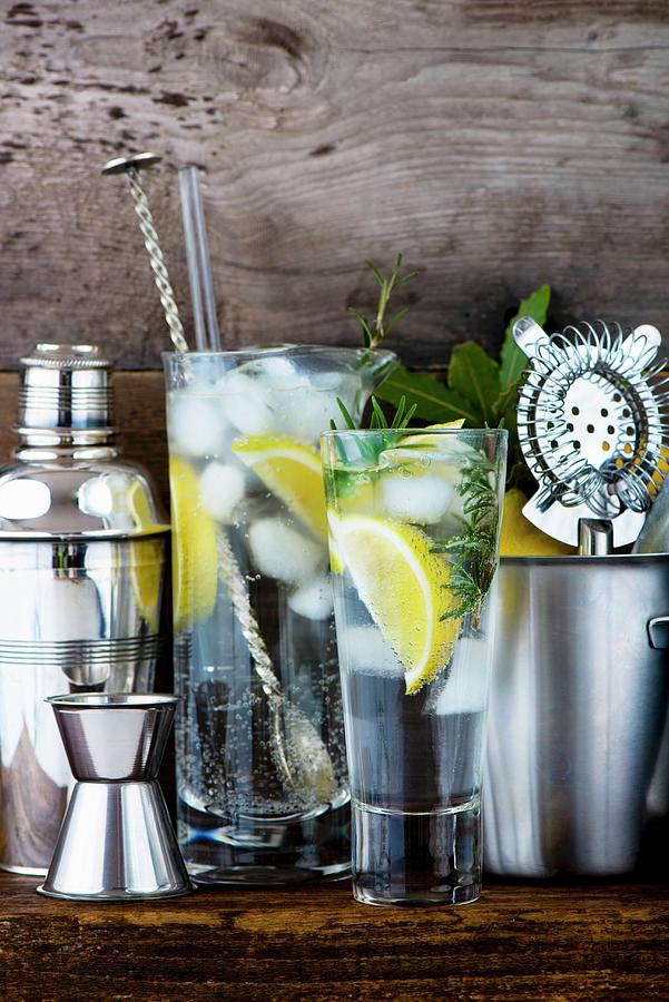 Gin And Tonic With Lemon, Ice Cubes And Rosemary Between Various Bar Utensils Photograph by Jamie Watson