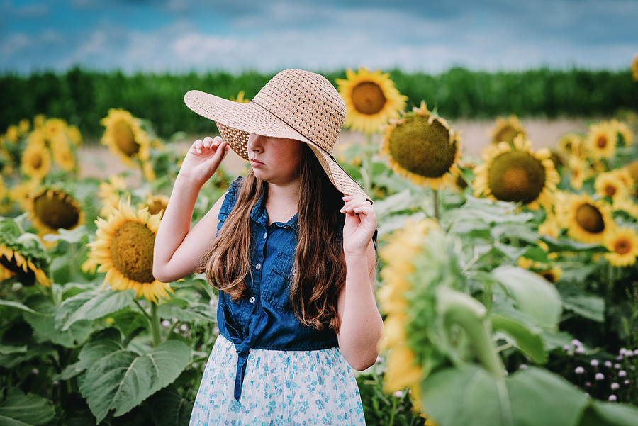Girl Putting On A Straw Hat In A Sunflower Field Photograph by