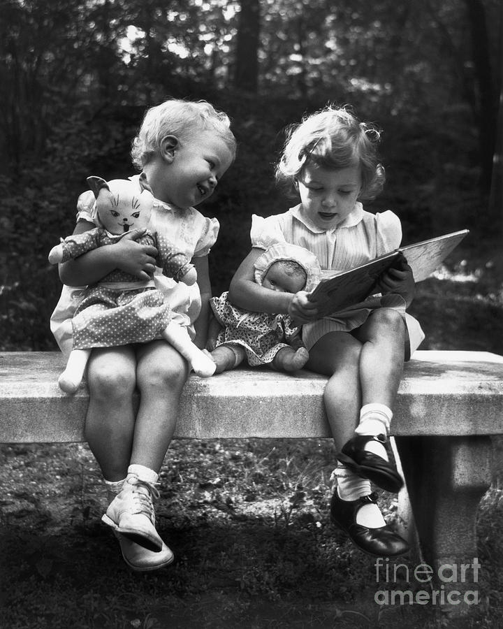 Girls Holding Dolls Seated On Bench Photograph by Bettmann