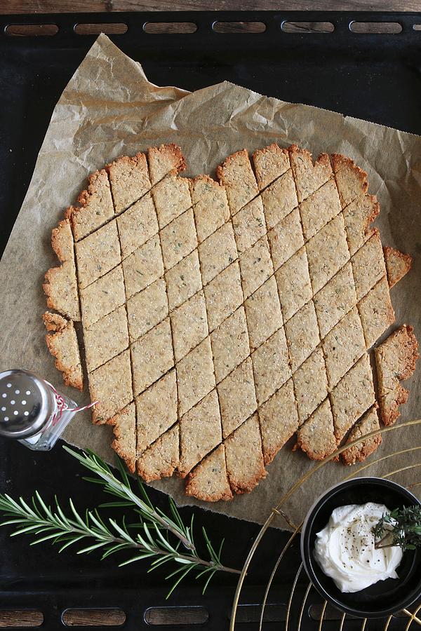 Gluten-free, Diamond-shaped Crackers With Rosemary And Sesame Seeds On A Baking Tray With A Bowl Of Dip And A Sprig Of Rosemary Photograph by Regina Hippel