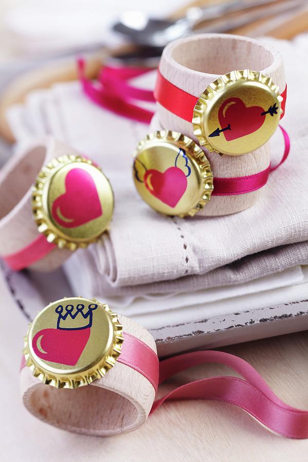 Gold Bottle Cap And Heart Motif And Pink Ribbons On Wooden Napkin Rings Photograph by Franziska Taube