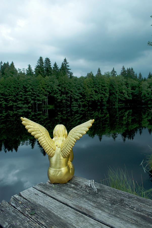Golden Angel Figurine Sat On Jetty Next To Lake In Woods Photograph by Matteo Manduzio