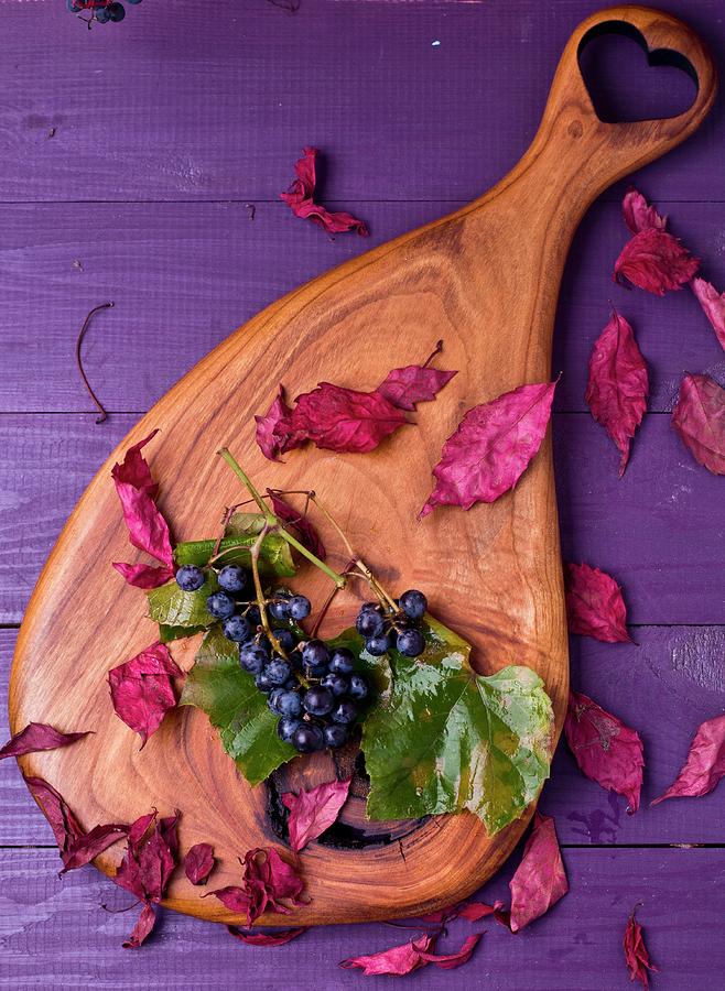 Grapes And Autumnal Leaves On A Wooden Board Photograph by Dorota Indycka