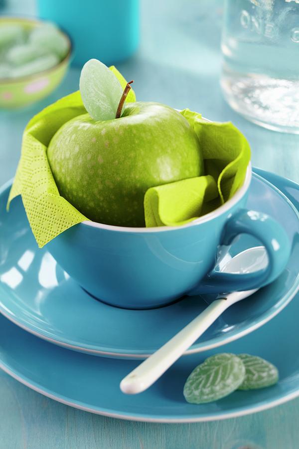 Green Apple In Blue Cup And Leaf-shaped Sweets On Plate Photograph by Franziska Taube