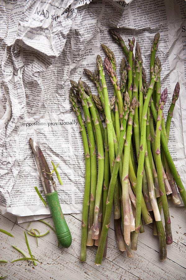 Green Asparagus And A Peeler On Newspaper Photograph by Studer, Veronika