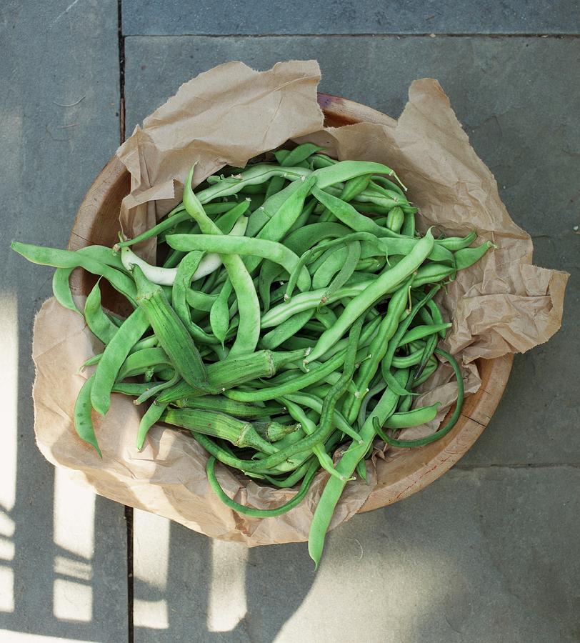 Green Beans And Okra Pods On A Piece Of Paper In A Wooden Bowl Photograph by Rene Comet