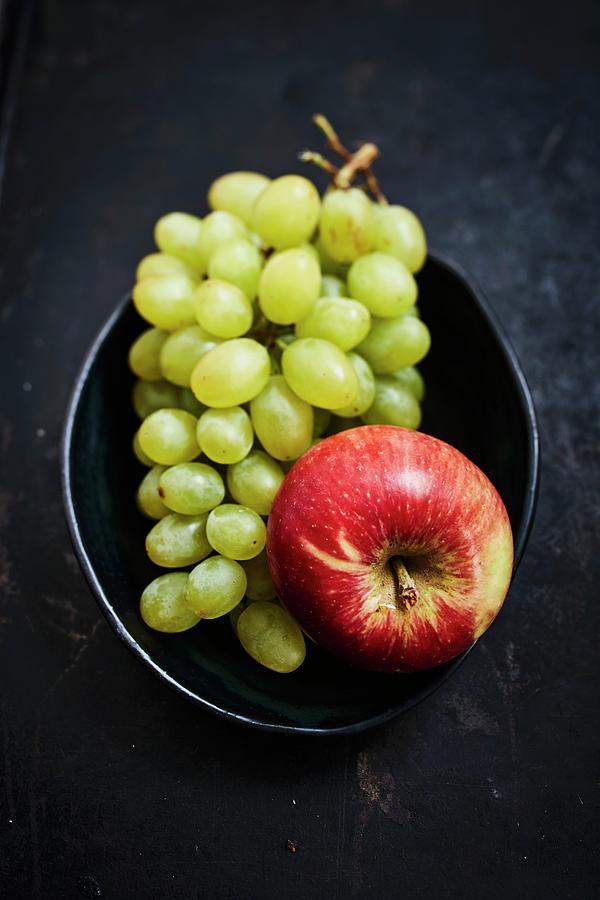 Green Grapes And An Apple In A Bowl On A Dark Background Photograph by Brigitte Sporrer