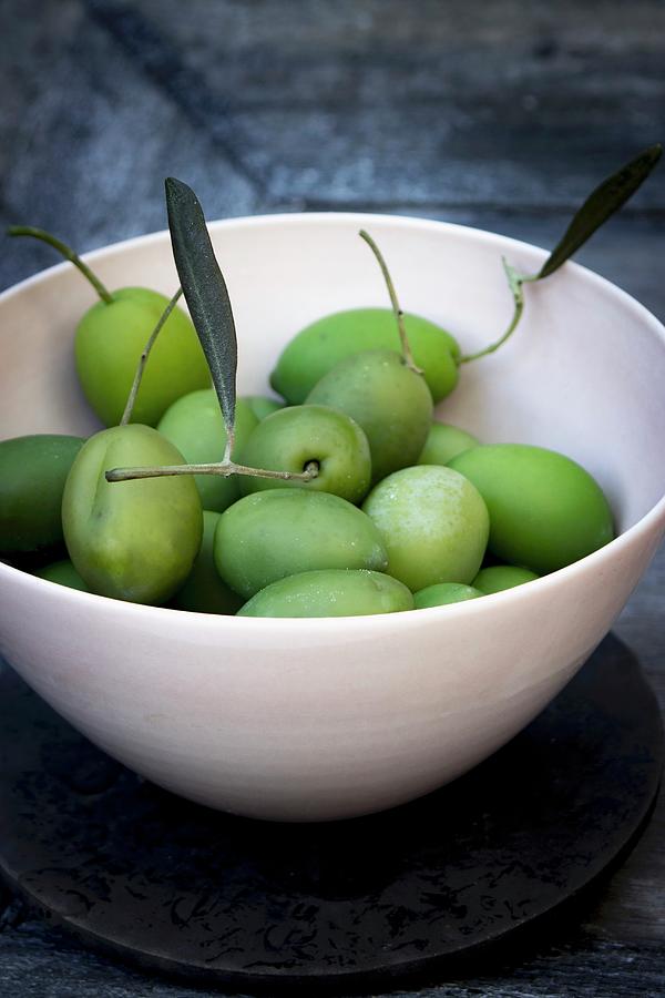 Green Olives With Stems And Leaves In A Bowl On A Grey Wooden Tray Photograph by Charlotte Von Elm