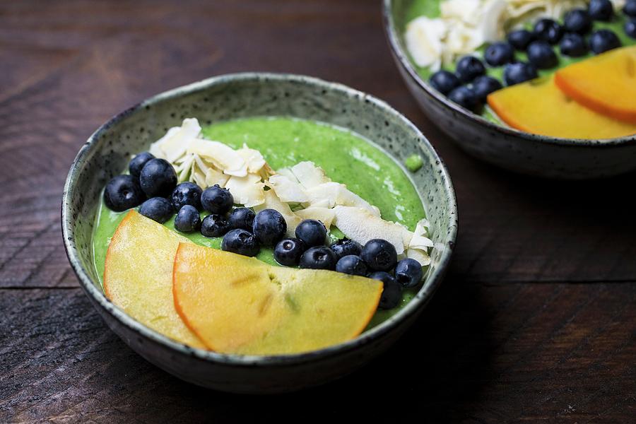Green Smoothies In Bowls With Blueberries, Coconut Flakes And Persimmon Slices Photograph by Nicole Godt
