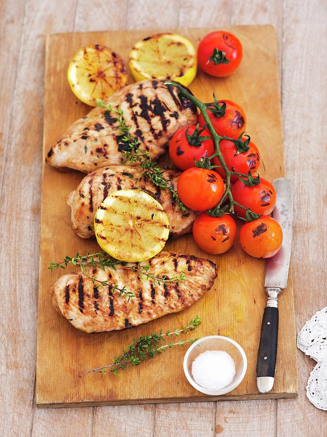 Grilled Chicken Breast, Lemons, Thyme And Tomatoes On A Wooden Board Photograph by Rua Castilho