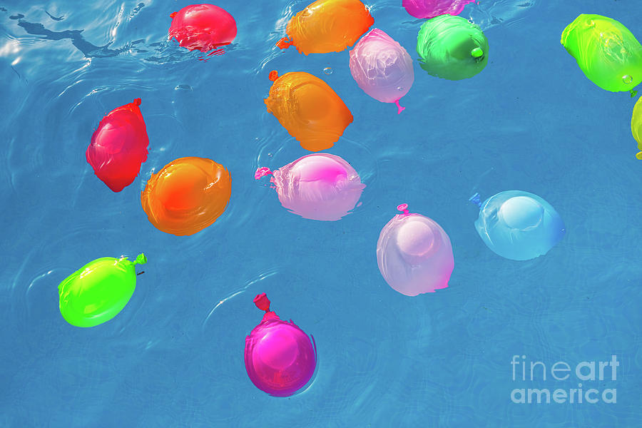 Group of many colorful plastic water balloons floating in the water of a pool to entertain their children on summer vacations. Photograph by Joaquin Corbalan