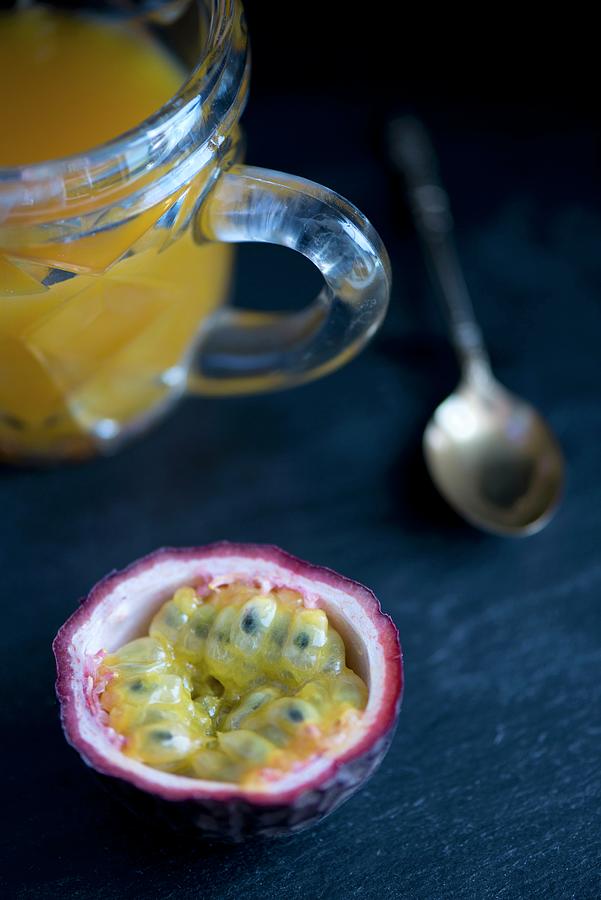 Half A Passion Fruit On A Black Slate Surface With A Spoon And A Jug Of Passion Fruit Juice In The Background Photograph by Jamie Watson