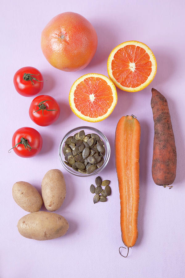 Halved Oranges, Carrots, Tomatoes, Potatoes And Seeds On Pink Background Photograph by Jalag / Annette Falck