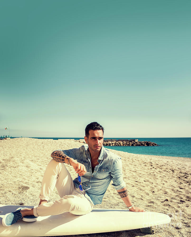Handsome Man Sitting On Surfboard At Beach Photograph