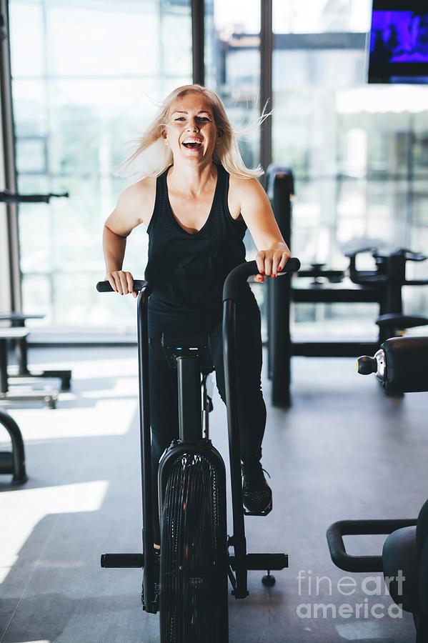 Happy woman riding an air bike at the gym. Photograph by Michal Bednarek