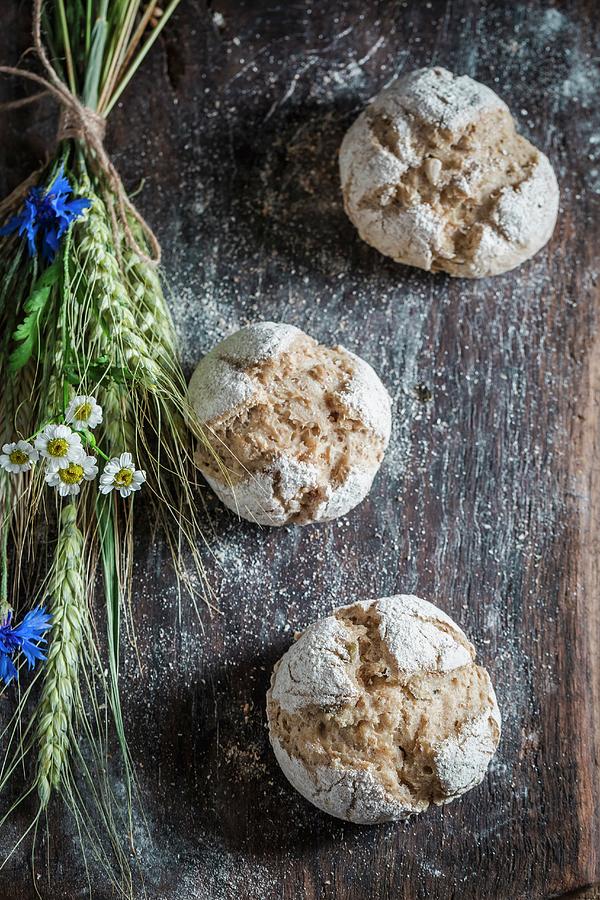 Healthy Wholemeal Buns With Ears Of Oat And Field Flowers On A Wooden Board Photograph by Shaiith