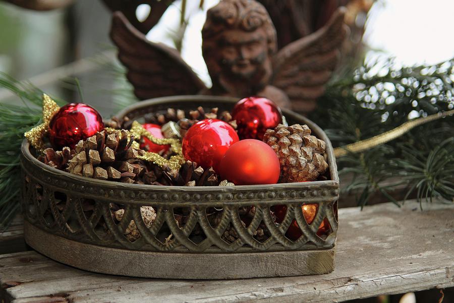 Heart-shaped Basket Filled With Pine Cones And Baubles In Front Of Iron Angel Figure Photograph by Barbara Ellger