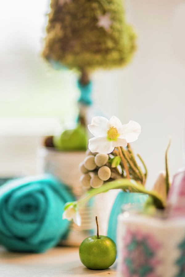 Hellebore Flowers, Green Apple, Turquoise Felt Flower And Small Tree Ornament In Blurred Background Photograph by Bildhbsch