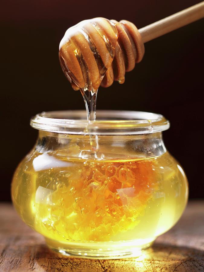Honey Dripping From A Honey Spoon Into A Jar Photograph by Foodcollection