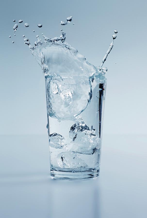 Ice Cubes Splashing Into A Glass Of Water With A Lemon Wedge Photograph by Krger & Gross