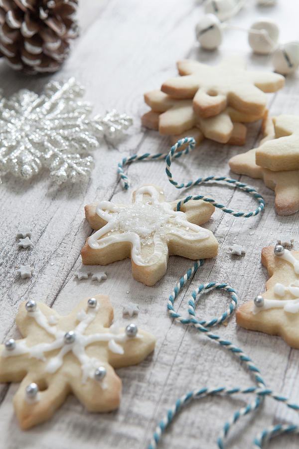 Iced Homemade Snowflake Shaped Christmas Biscuits Being Treaded With Blue And White Bakers Twine On A White Wash Wooden Surface Surrounded By Christmas Tree Decorations Photograph by Stacy Grant