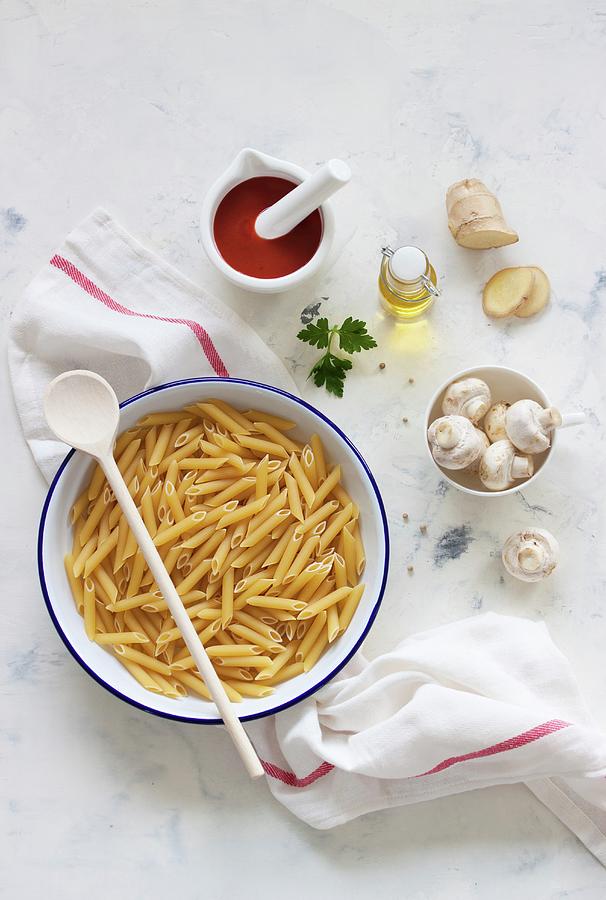 Ingredients For A Pasta Dish: Penne, Mushrooms, Sieved Tomatoes, Olive Oil And Ginger Photograph by Valeria Aksakova