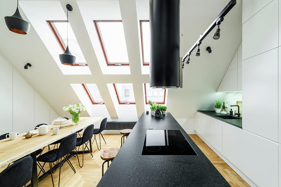 Island Counter And Dining Table With Black Chairs In High-ceilinged Room With Skylights In Sloping Wall Photograph by Lukasz Zandecki