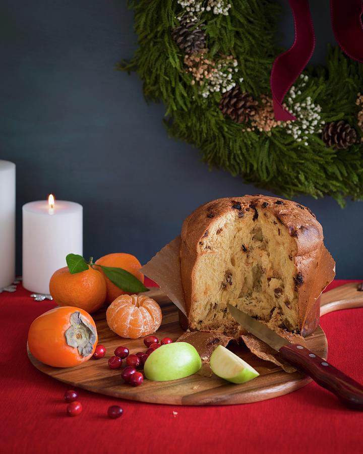 Italian Panettone Cut Open On A Cutting Board With Fruit On A Red Tablecloth With White Candles And A Wreath In The Background Photograph by Don Crossland