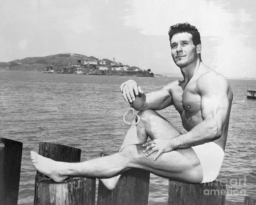 Jack Lalanne Sitting On Post Near Water Photograph by Bettmann