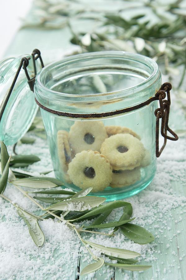 Jam Sandwich Biscuits In An Old Flip-top Jar With Olive Sprigs And Snow Photograph by Martina Schindler