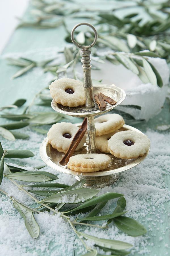 Jam Sandwich Biscuits On A Cake Stand Between Olives Sprigs On A Table Covered With Snow Photograph by Martina Schindler