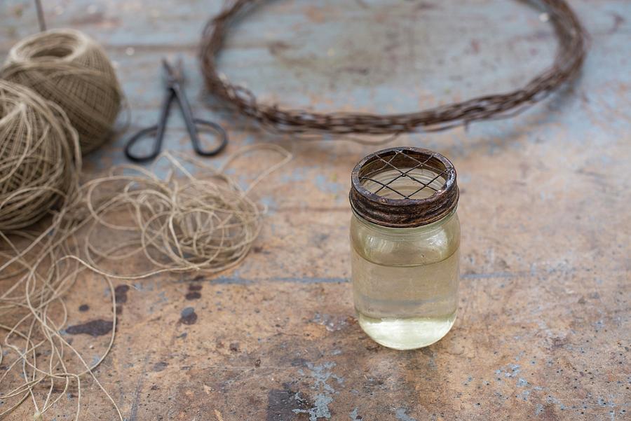 Jar Of Water With Metal Lid In Front Of Parcel String And Wire Wreath Photograph by Irene Berni