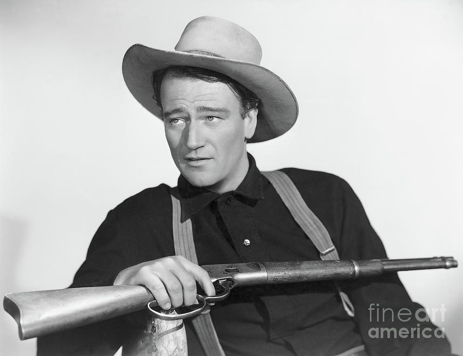 John Wayne Seated With Rifle Photograph by Bettmann