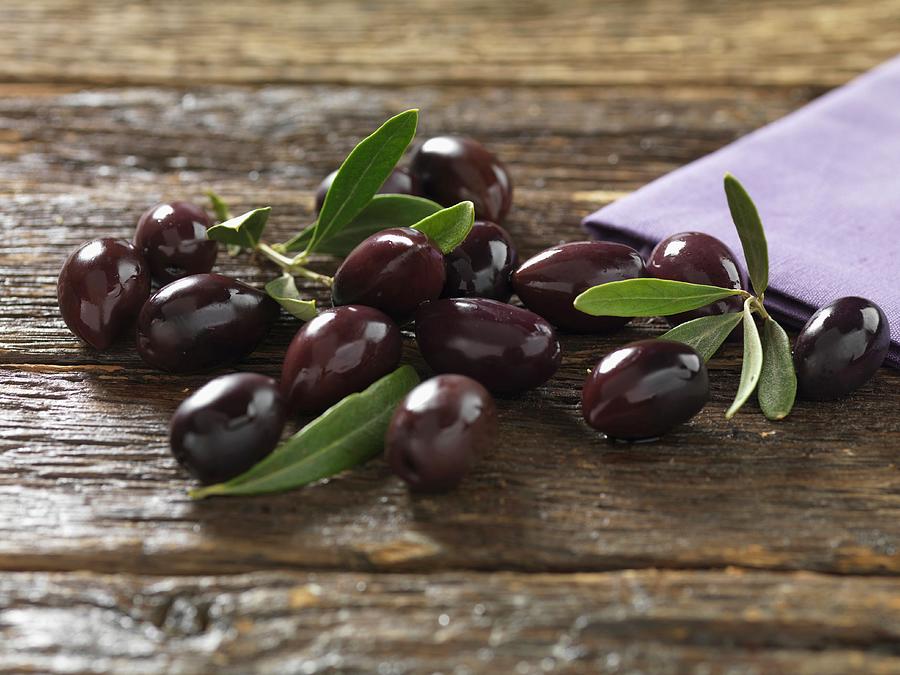 Kalamata Olives With Leaves On A Wooden Surface Photograph by Robert Morris