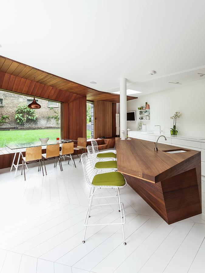 Kitchen Counter In Exotic Wood And Bauhaus-style Bar Stools; Large Windows In Background With Long Glass Table And Pale Wooden Chairs Photograph by Simon Maxwell Photography