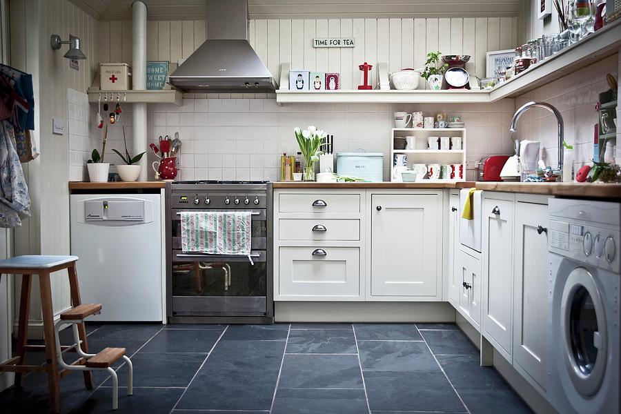 Kitchen With White Furniture, Fitted Appliances And Utensils On Wall-mounted Shelf Photograph by George Blomfield