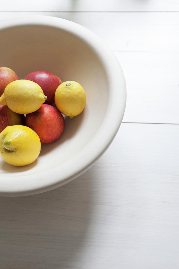 Lemons And Apples In White Fruit Bowl On White Table Photograph by Anne-catherine Scoffoni
