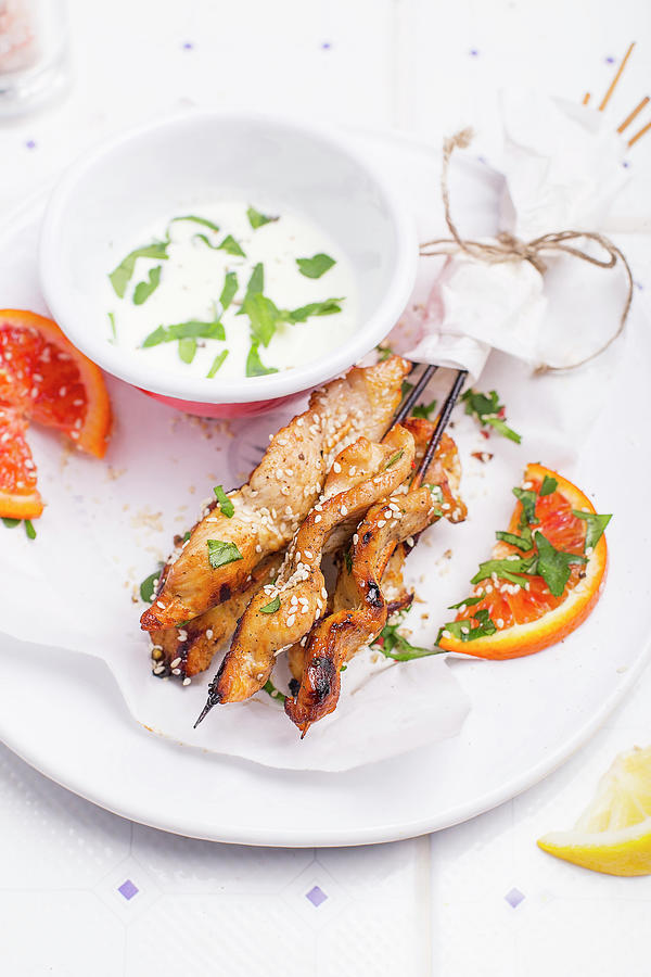 Lemony Marinated Chicken Skewers On A White Plate, Served With Sesame Seeds, Orange Pieces And Fresh Herbs Photograph by Natalia Mantur
