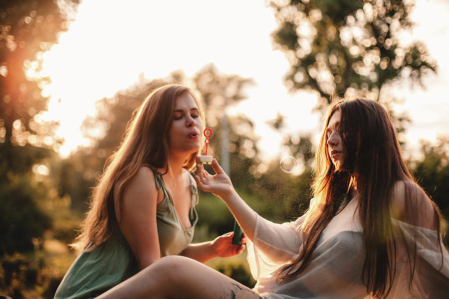Lesbian Couple Playing With Bubbles While Relaxing In Park In Summer