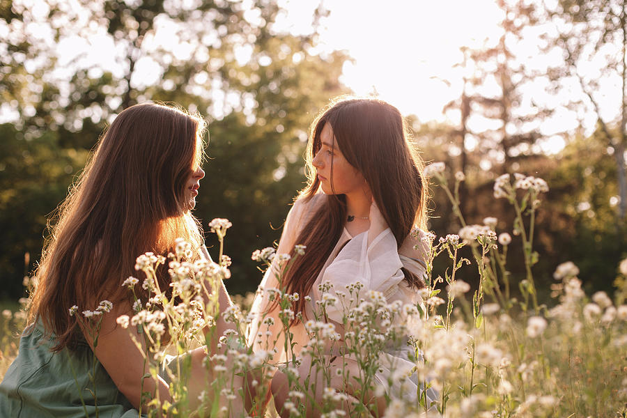 Lesbian Couple Talking Sitting Amidst Flowers In Summer Forest Photograph By Cavan Images Fine