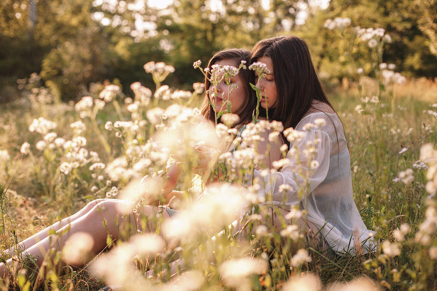 Lesbian Couple Talking Sitting Amidst Flowers On Summer Field Photograph By Cavan Images