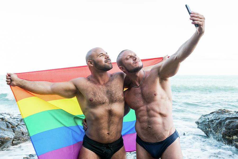 Summer Photograph - Lgbt Pride Concept. Gay Bear Couple Holding Rainbow Flag With Open Arms Taking A Selfie Photo. by Cavan Images