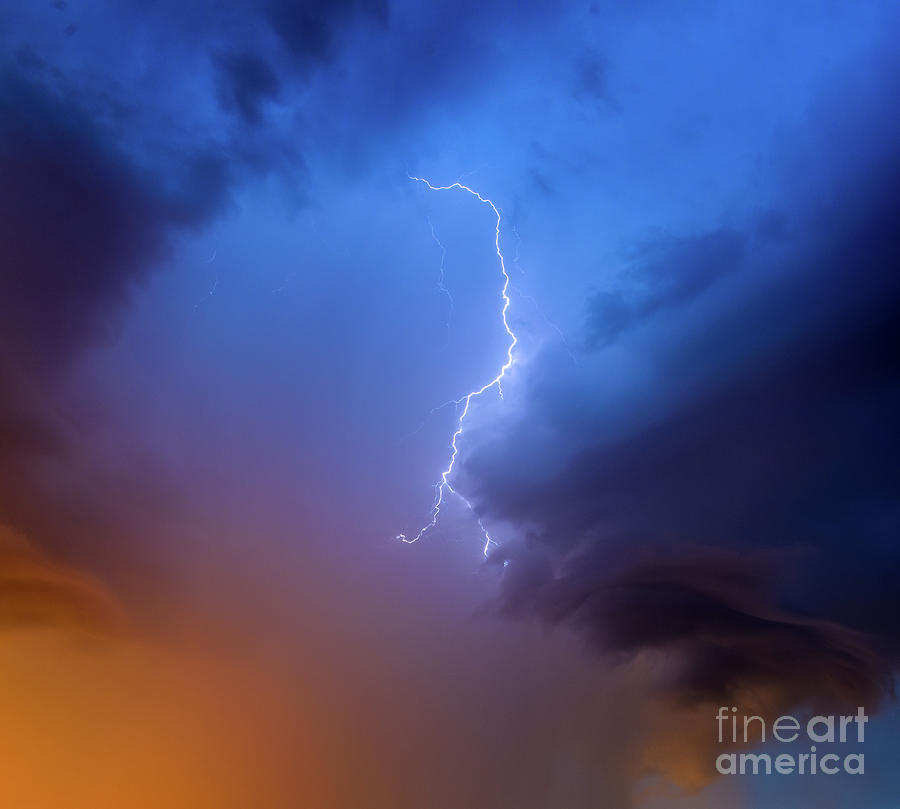 Lightning strikes high up in  the dramatic dark blue stormy sky at dawn. Photograph by Ulrich Wende