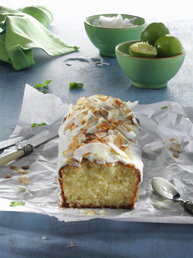 Lime And Coconut Cake, Sliced, On A Piece Of Paper On A Blue Wooden Table Photograph by Christian Schuster