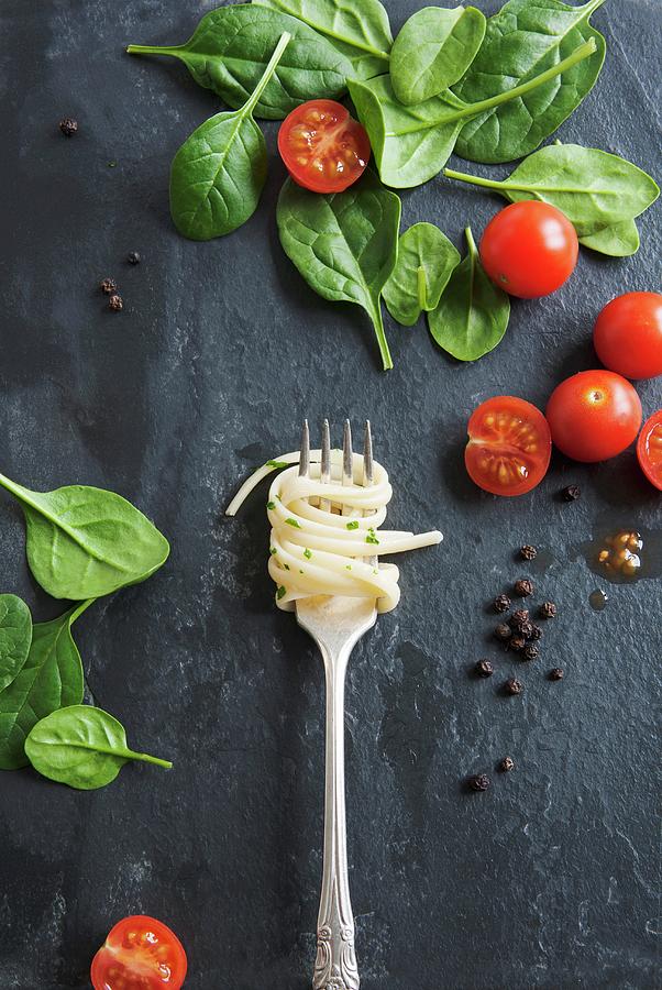 Linguine On A Fork On A Marble Table, With Tomatoes And Spinach Leaves Photograph by Victoria Firmston