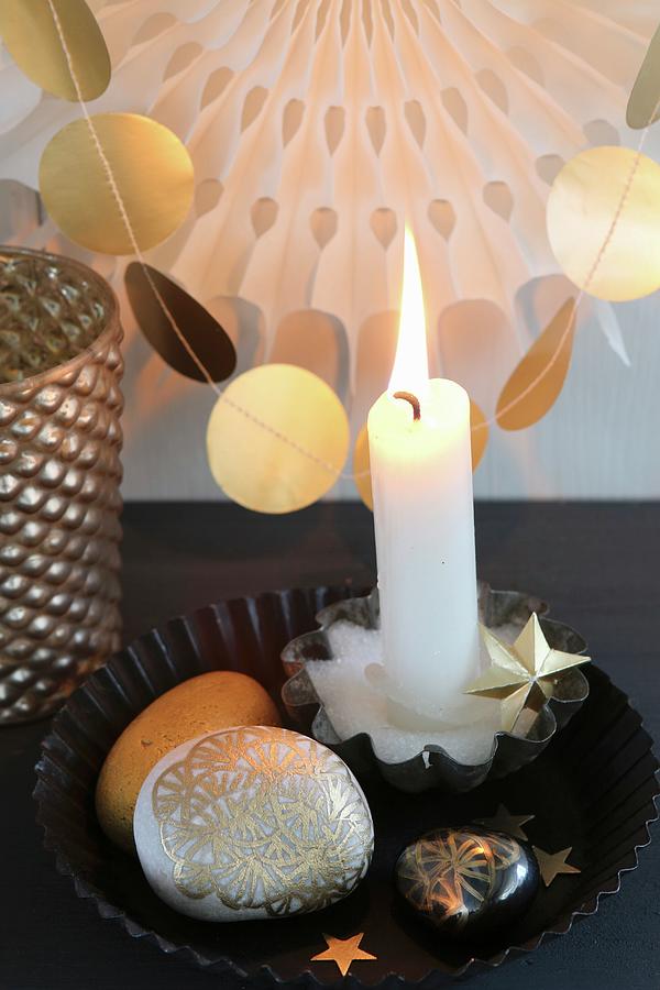 Lit Candle And Gold-painted Pebbles In Black Cake Tin In Front Of Garland Of Gold Paper Discs Photograph by Regina Hippel