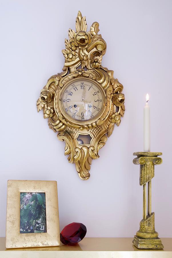 Lit Candle In Brass Candlestick On Surface And Gilt-framed Wall Clock On Pastel Wall Photograph by Blickpunkte
