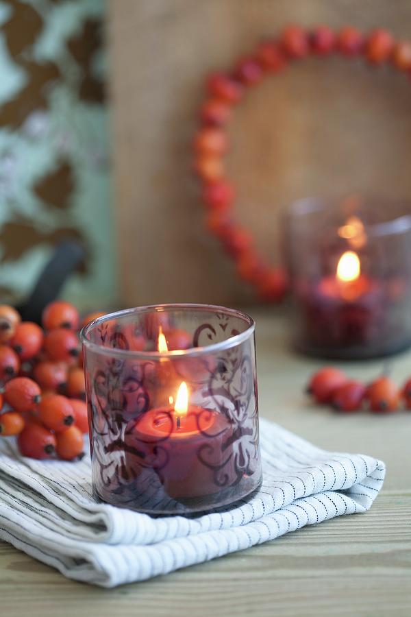 Lit Candle In Tealight Holder With Painted Pattern In Front Of Rose Hip Posy And Rose Hip Wreath Photograph by Martina Schindler