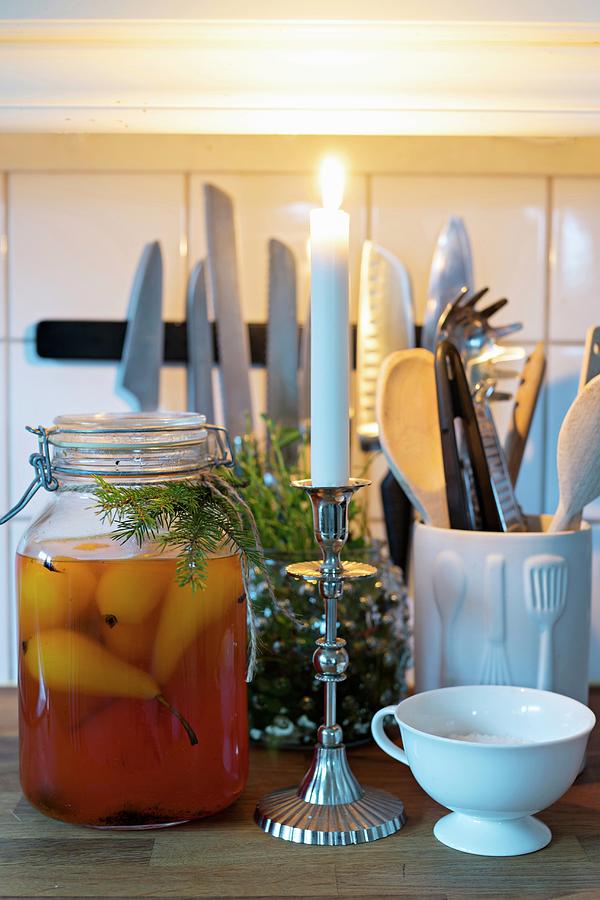 Lit Candle, Pears In Preserving Jar And Arrangement Of Fir Twigs In Front Of Kitchen Utensils Photograph by Cecilia Mller