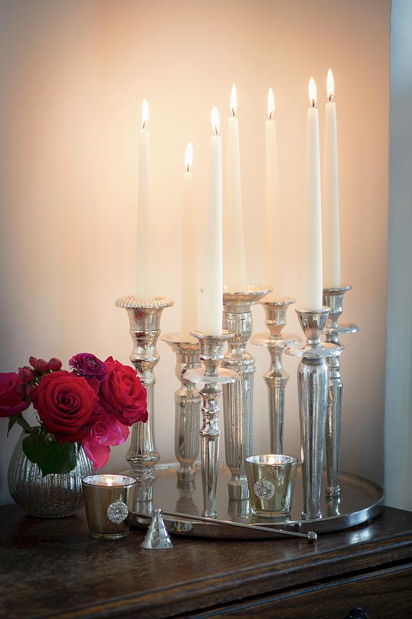 Lit Candles In Various Silver Candlesticks On Tray And Small Vase Of Roses Photograph by Winfried Heinze